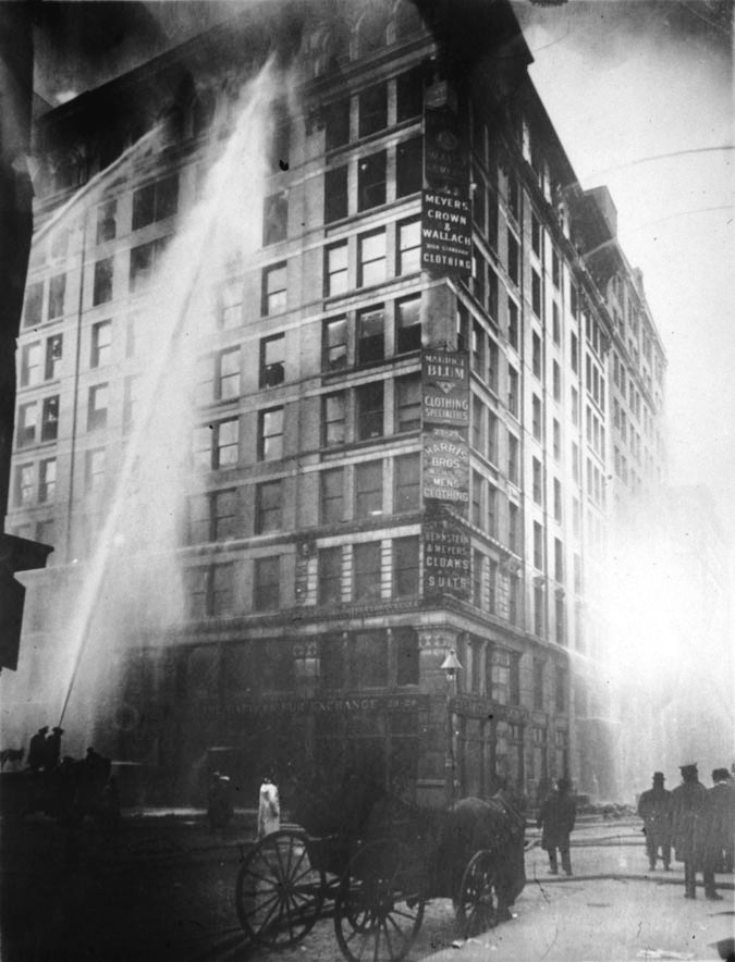Historic photograph of the Triangle Shirtwaist Factory fire in 1911, showing crowds gathered on the street below the burning building in New York City
